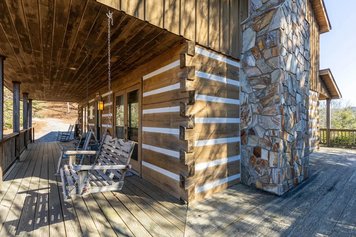 A welcoming wooden deck features classic rocking chairs and a stone chimney, offering a cozy spot to relax and take in the surrounding forest and mountain vistas. The ambiance is serene, ideal for family gatherings after a day out.