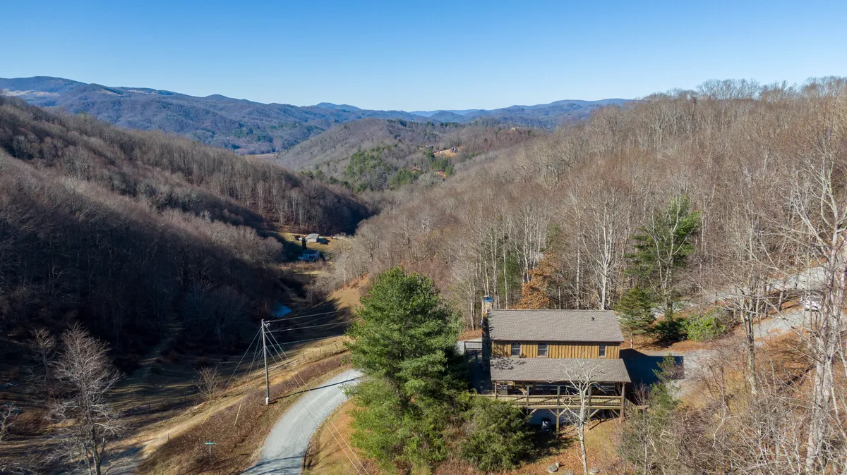 This image captures Windsong cabin nestled atop a mountain, surrounded by rolling peaks and lush forest. The winding road hints at accessibility, while the setting conveys a sense of peaceful seclusion and adventure. The scene is bathed in natural light, emphasizing the panoramic views available from the property.