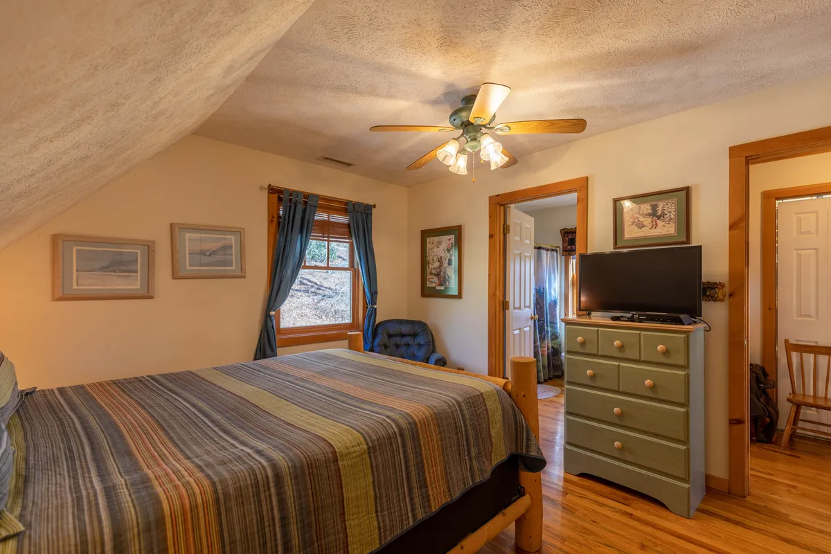 A comfortable Queen bedroom featuring striped bedding, wooden furniture, a blue chair, and a television, all illuminated by natural light for a welcoming ambiance.