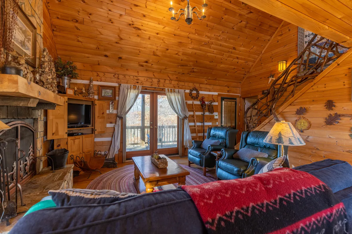 A cozy living space featuring a fireplace, large windows that frame the scenic views, comfortable seating, and rustic wooden beams. The atmosphere suggests a warm retreat after time spent outdoors.